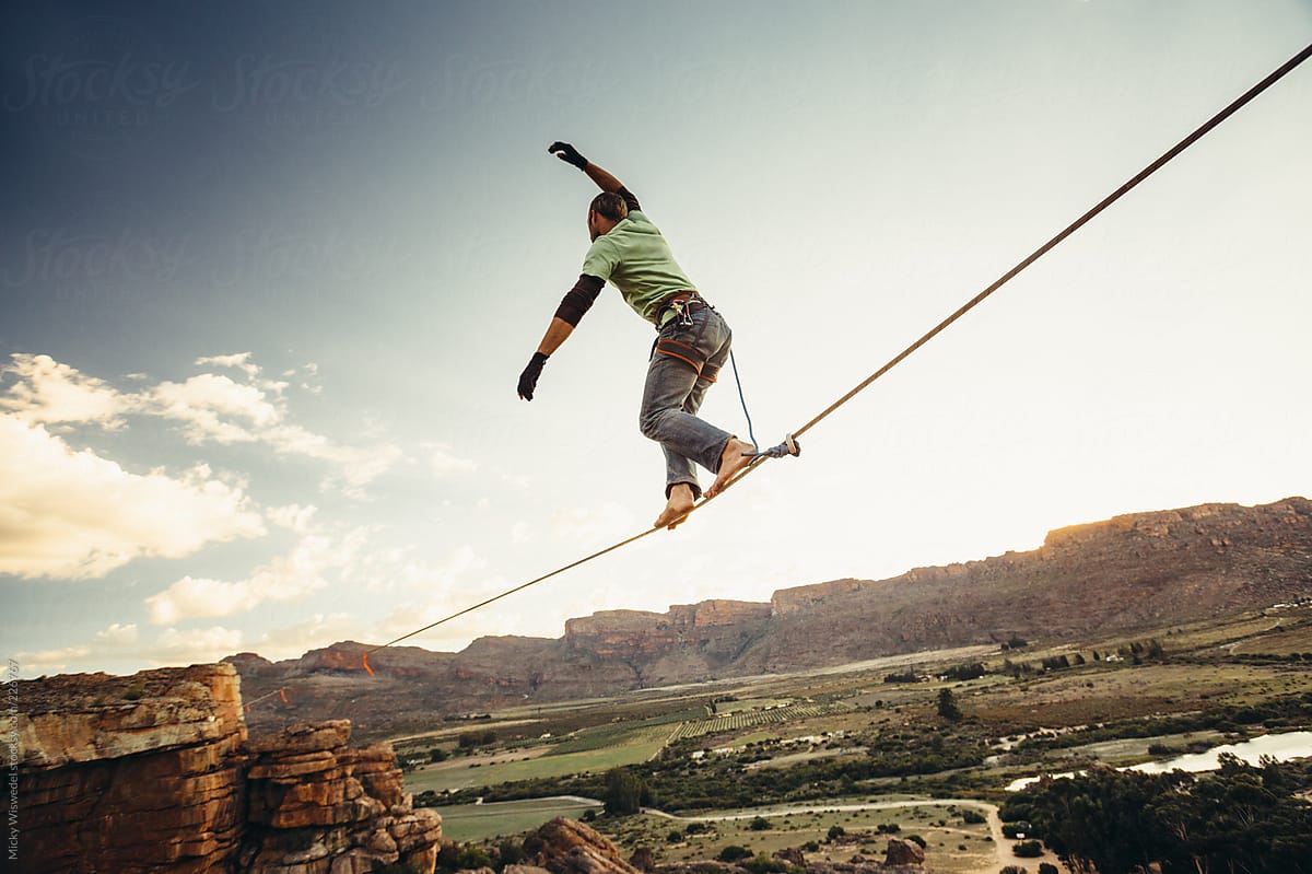 Man Balance Walking On A Highline Or Tight Rope High Over A Mountain Valley  At Sunset by Stocksy Contributor Juno - Stocksy
