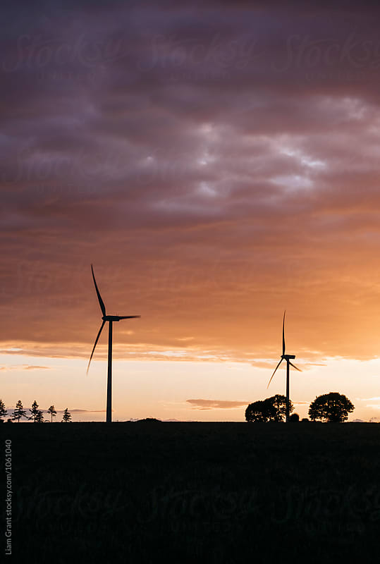 Wind turbine silhouetted against orange cloud at sunset. Norfolk, UK.