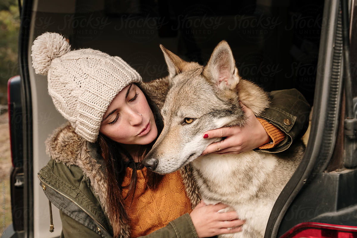 Young woman in camper van petting a cute  wolf dog in the mountain