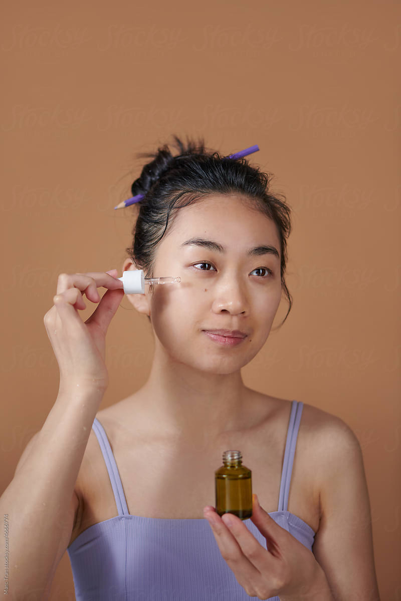 Portrait shot of young asian woman applying serum or essential oil