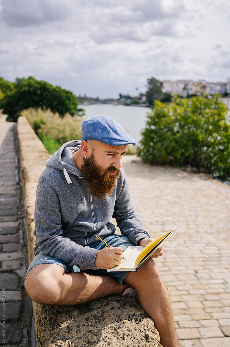 Man painting in notebook while sitting on riverside