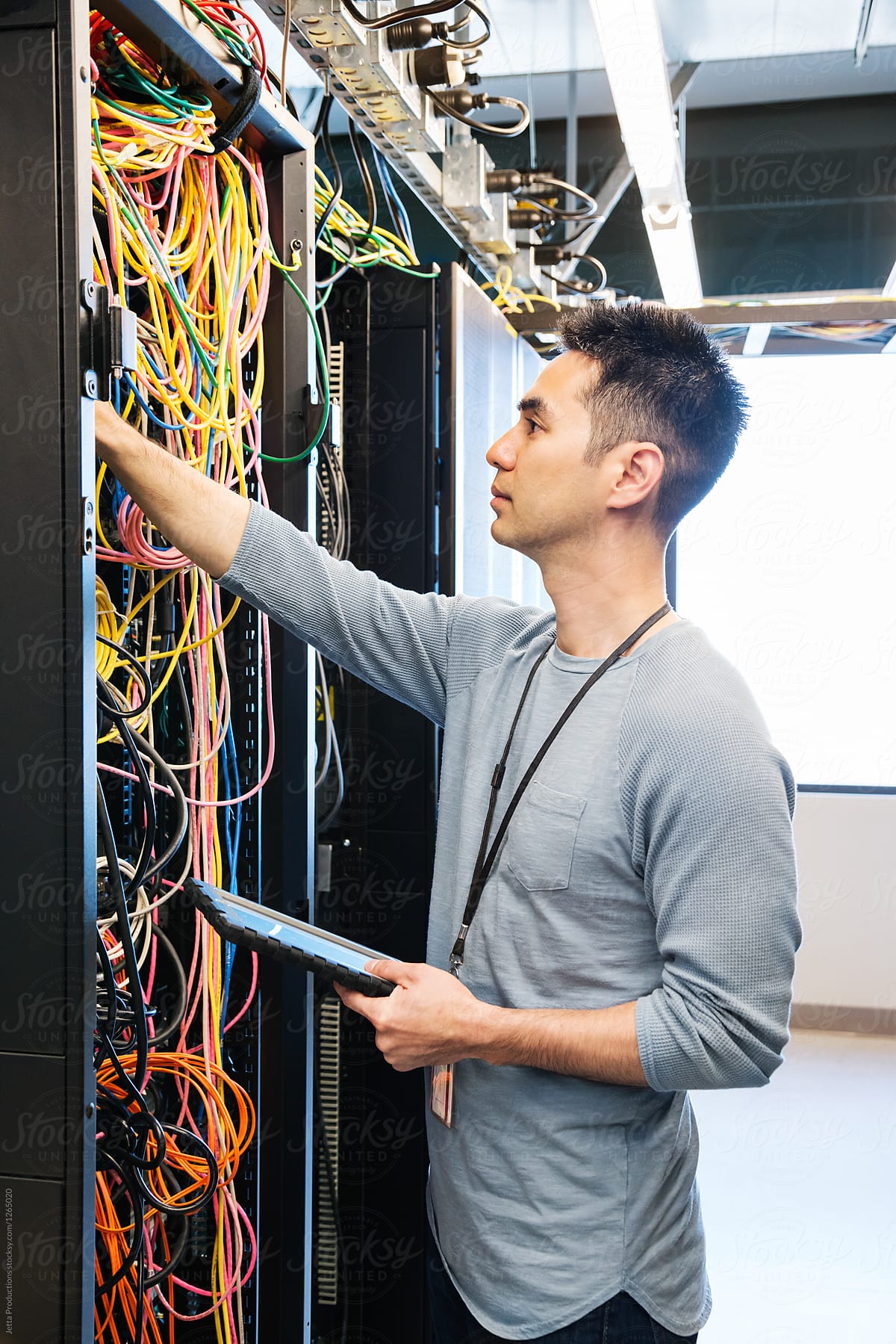 Asian technician reaches in amongst the cables inside a server a