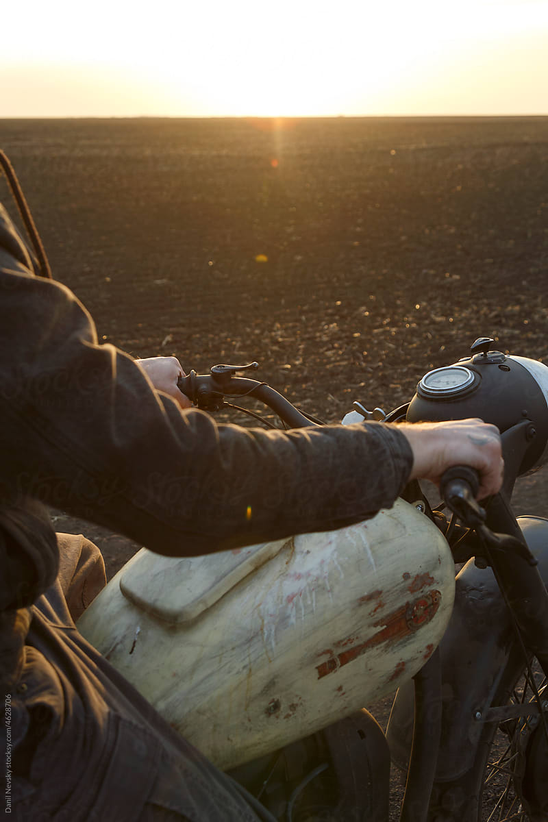 Crop motorcyclist driving motorbike at sunset
