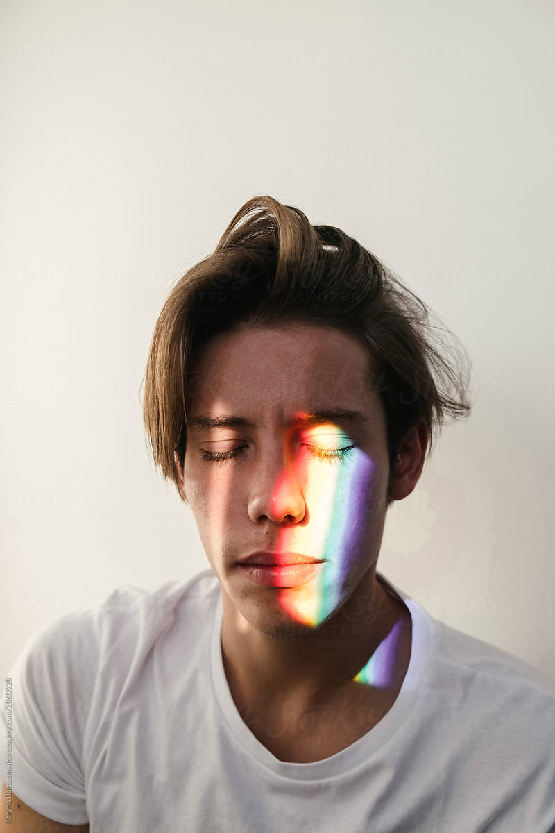 portrait of a charming guy with long hair and eyes closed with a strip of rainbow light on his face