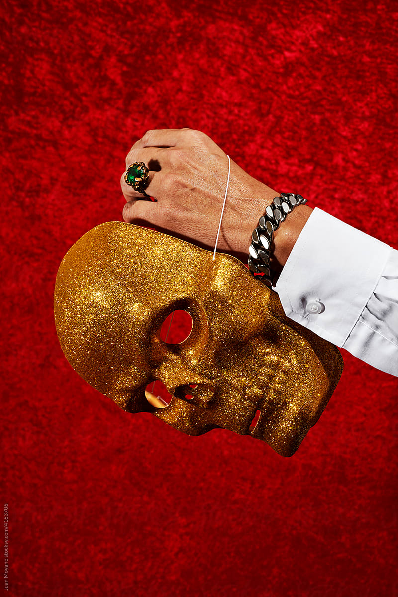 man holding a golden glitter skull mask