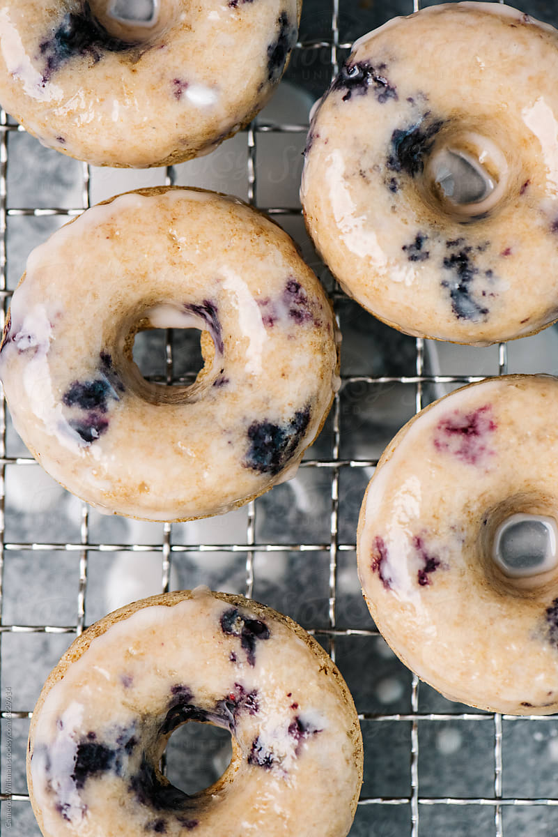 Baked and glazed blueberry donuts drying on a rack
