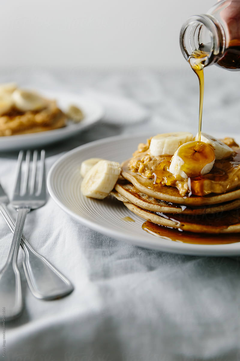 Pouring maple syrup on vegan pancakes with peanut and banana