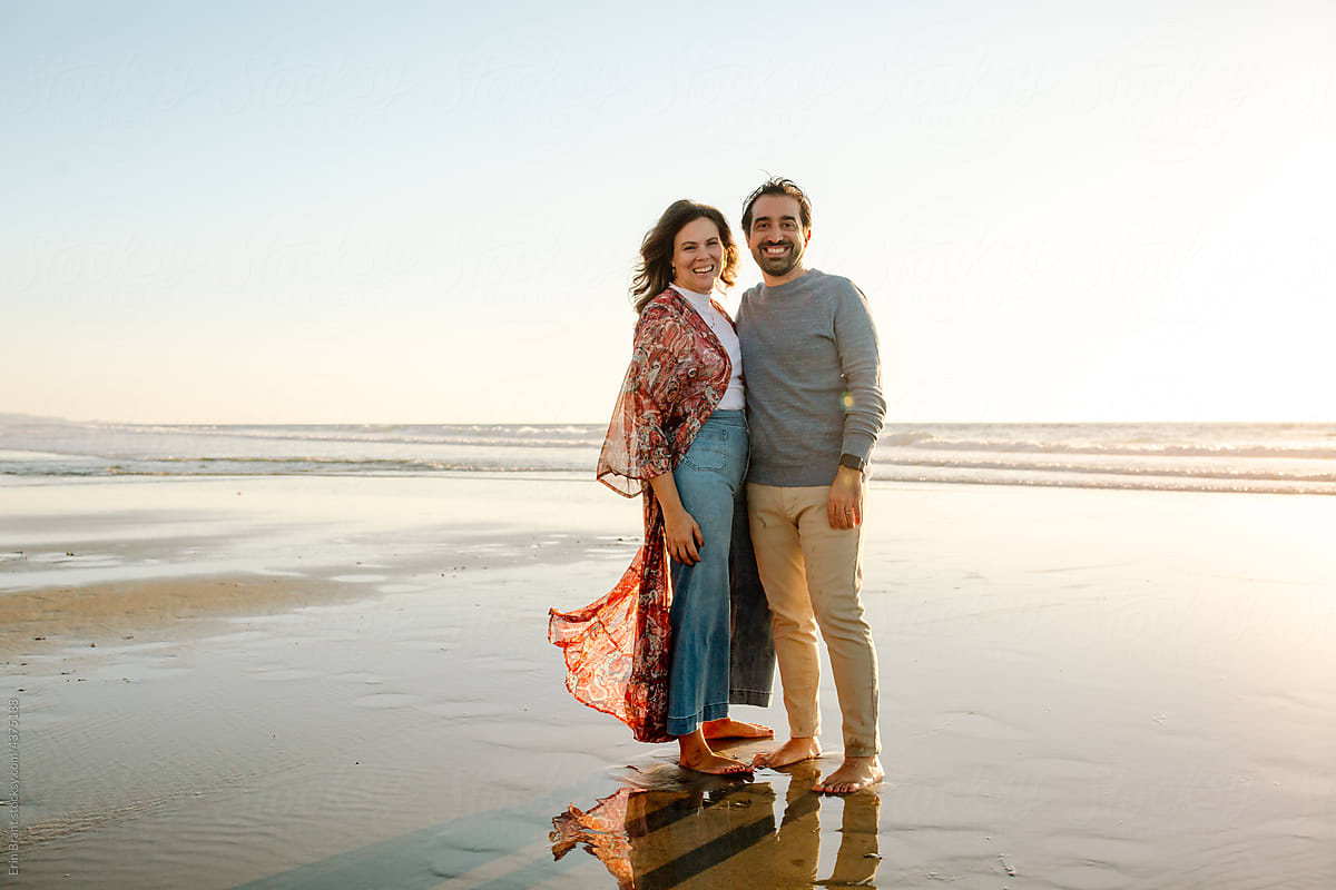 Barefoot couple standing on beach at sunset