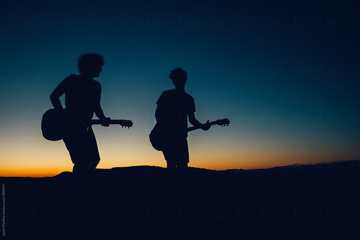 silhouette of two friends playing guitar at sunset