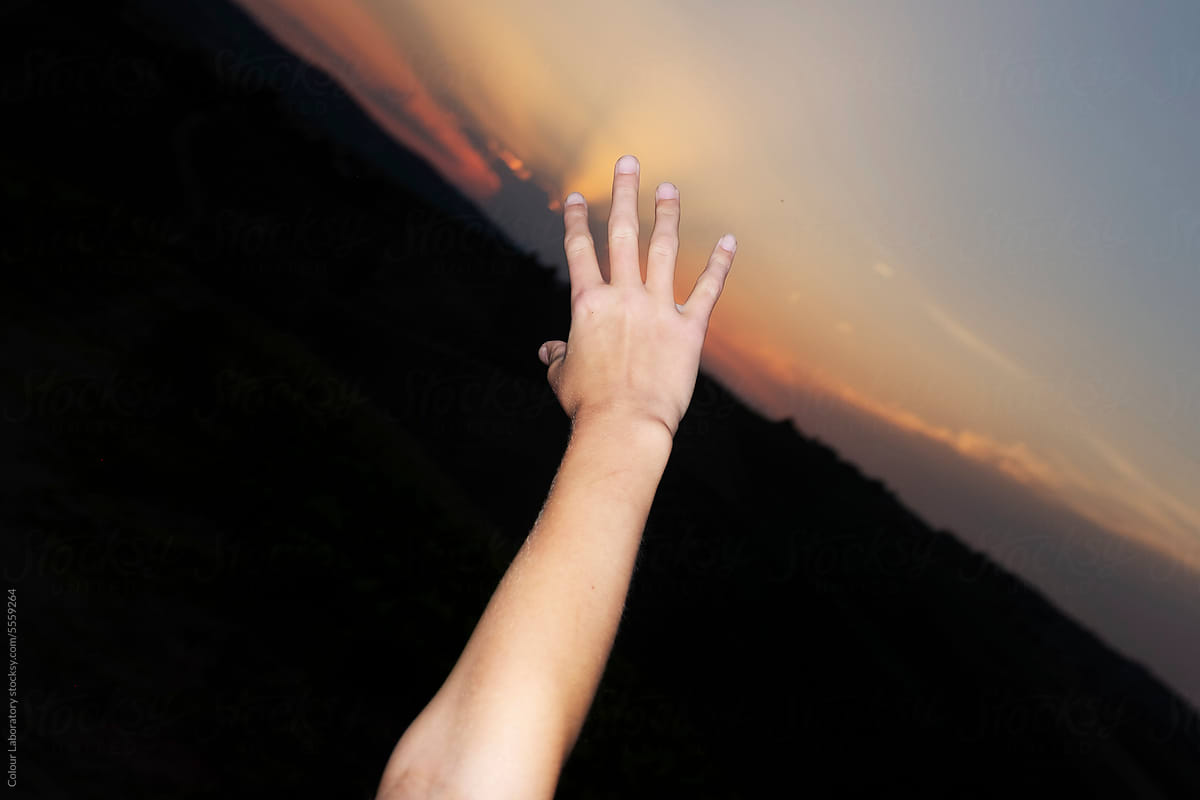 Hand reaching toward sunset