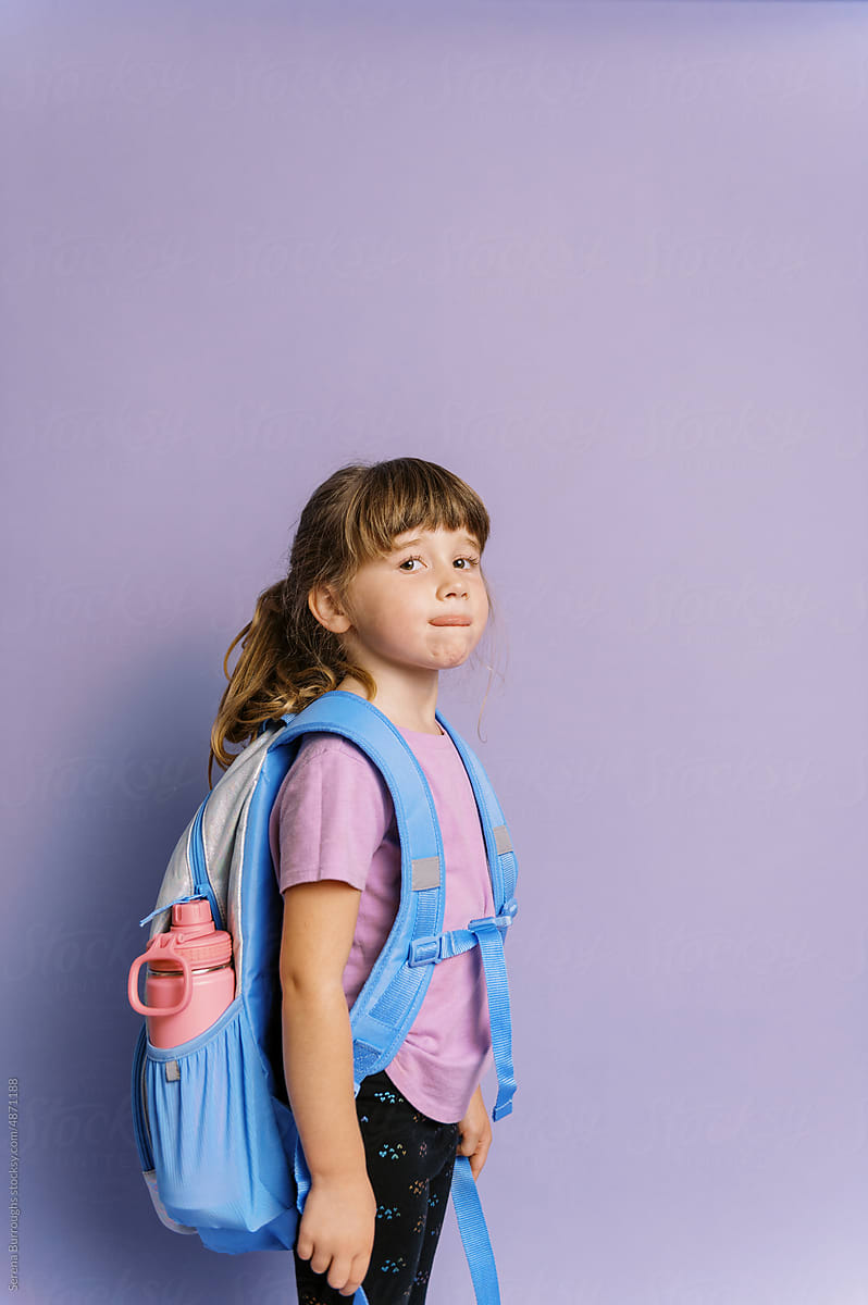 girl in front of purple background wearing her backpack for school