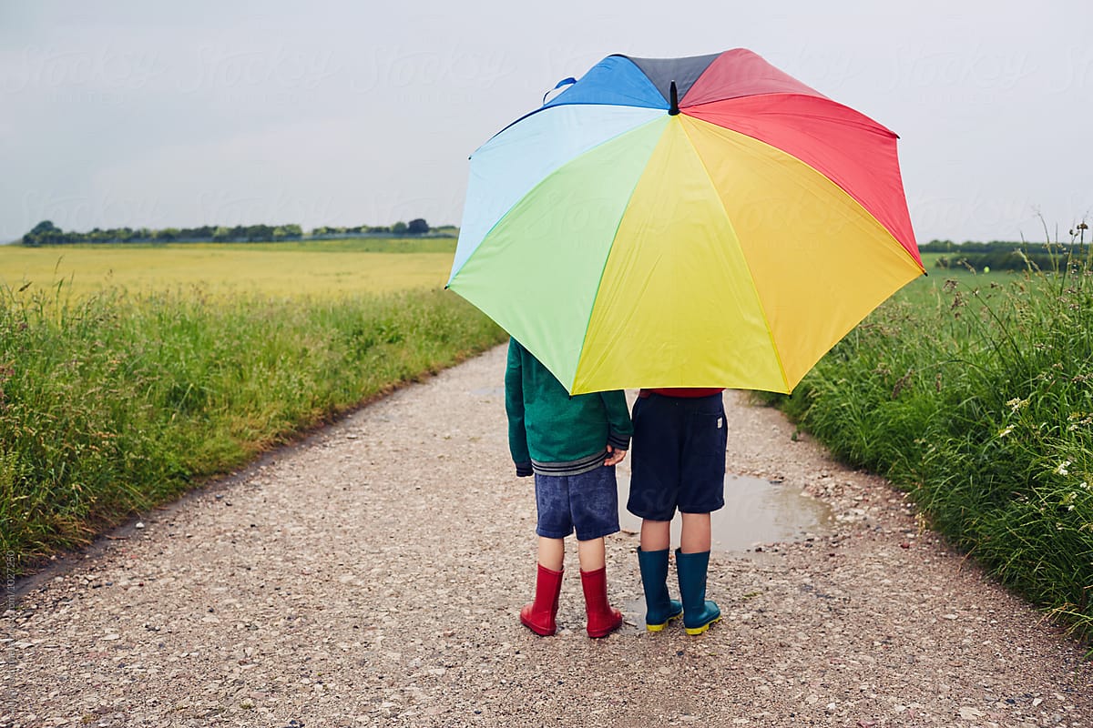 Children walking on a rainy day with a rainbow umbrella