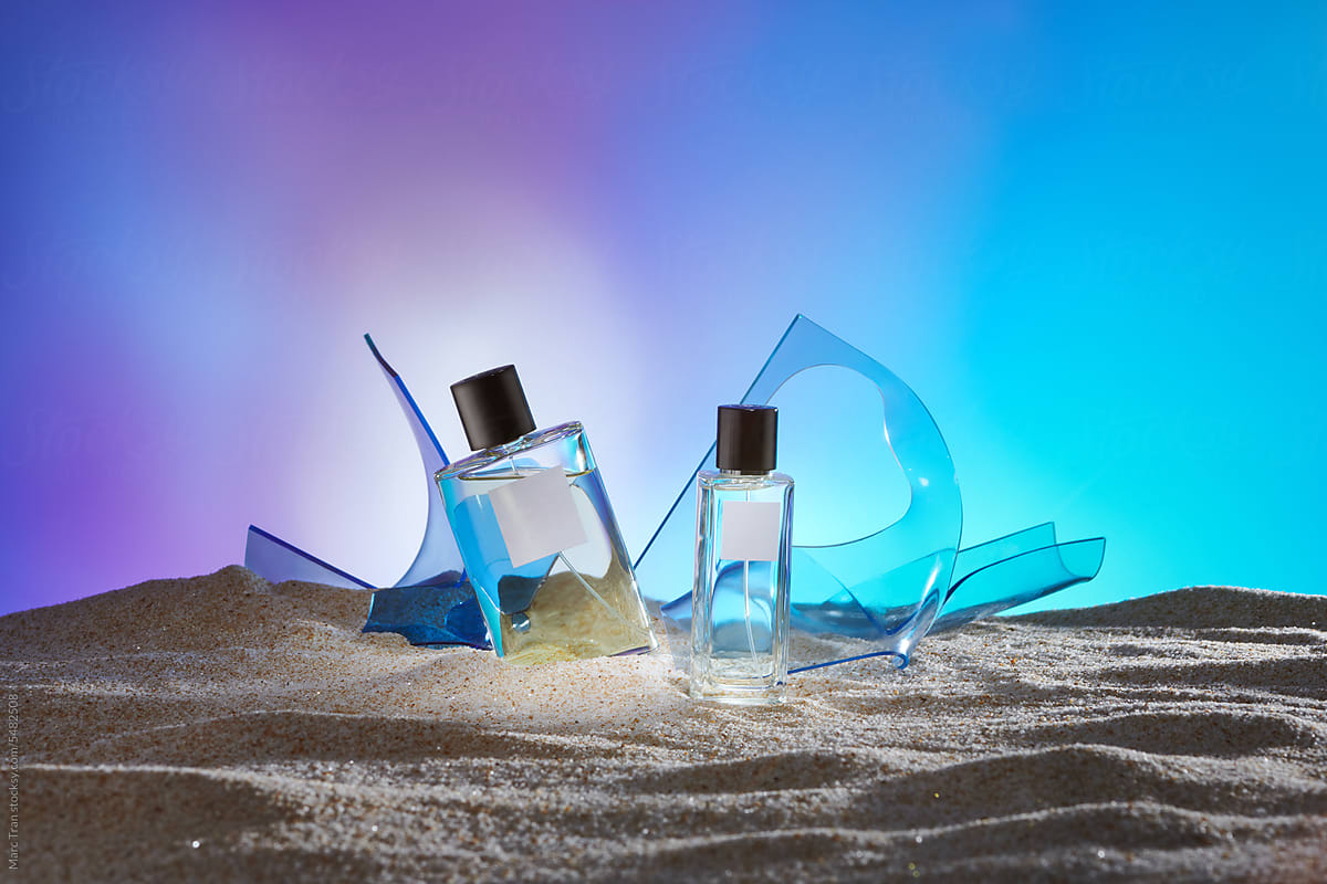 Two perfume bottles are displayed on sand with back light