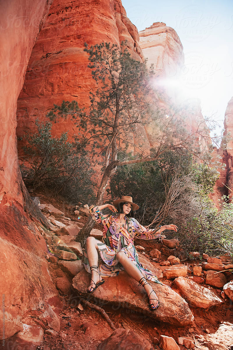 Stylish Cowgirl in dress sits on desert rocks.
