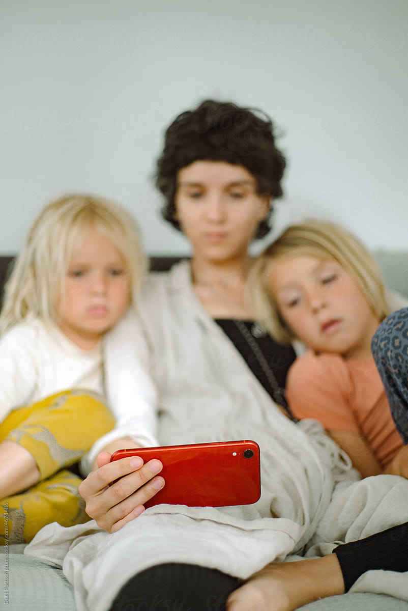 Two boys and an adult woman are watching cartoons on a smartphone.