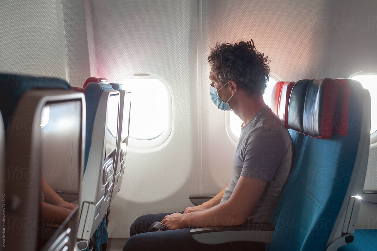 passenger wearing face mask in airplane, travel during covid 19 pandemic of coronavirus