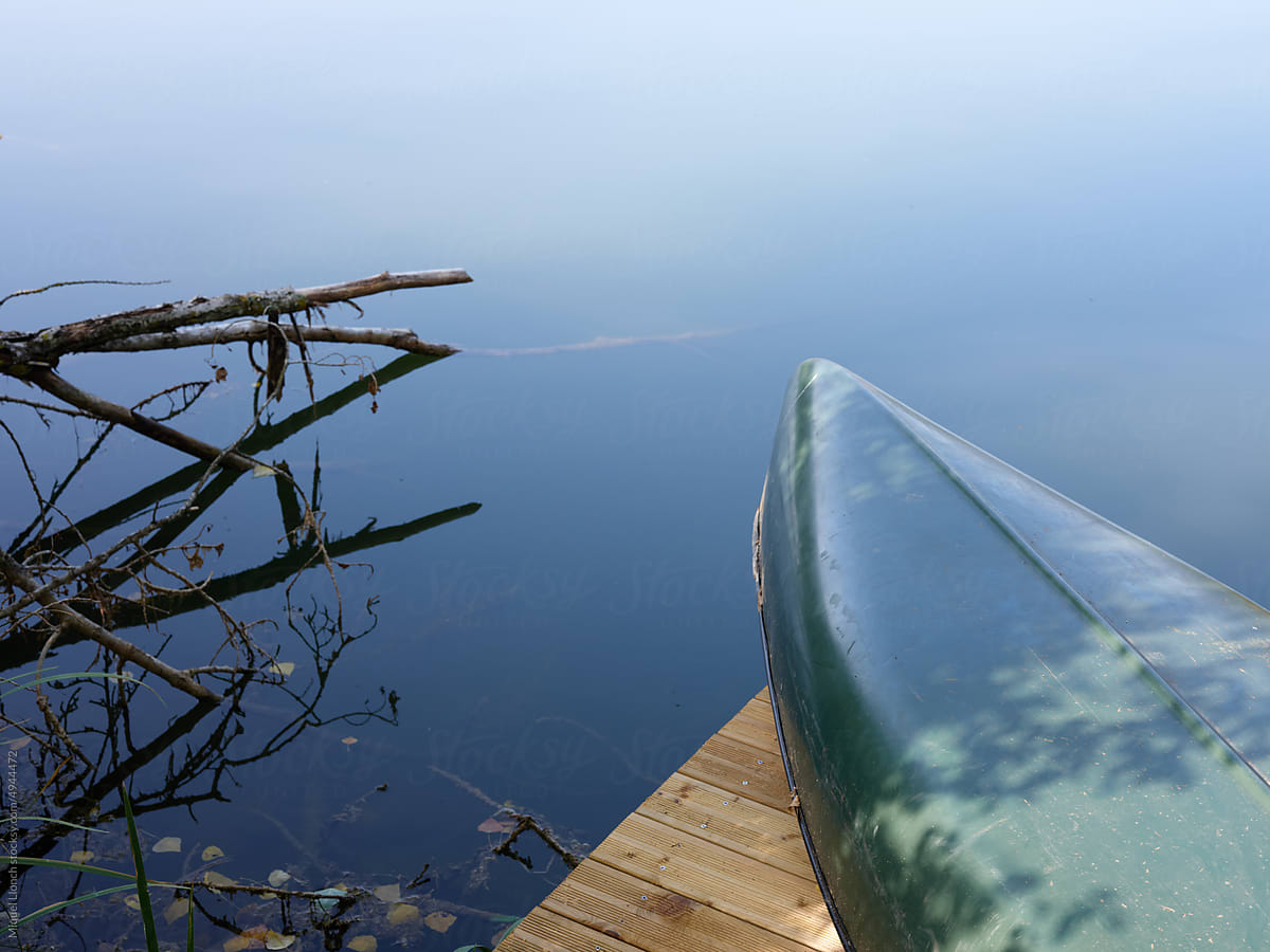 Cropped green canoe on the wooden deck of a dark blue lake
