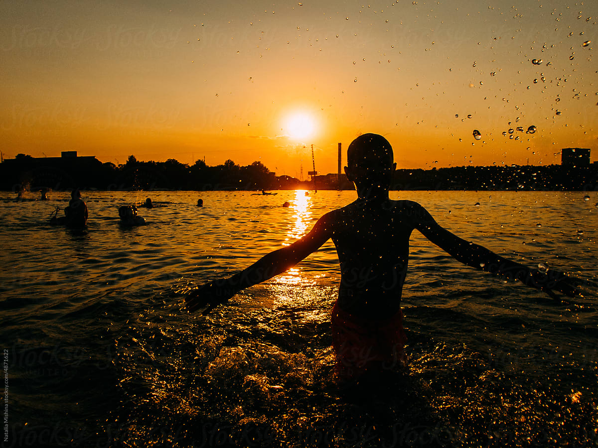 A boy swims in a city pond, sunset.
