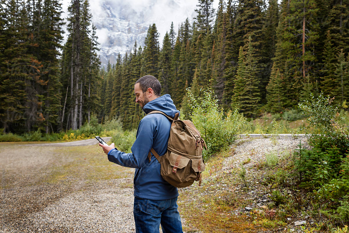Young man with backpack using a phone in the middle of the forest, Canadian Rockies