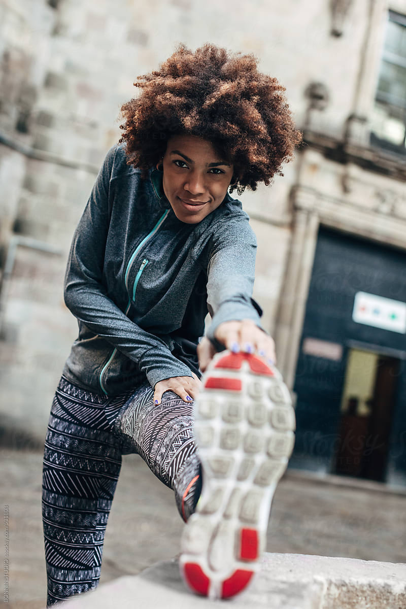 young-afro-woman-doing-stretching-exercises-on-the-street-by-stocksy