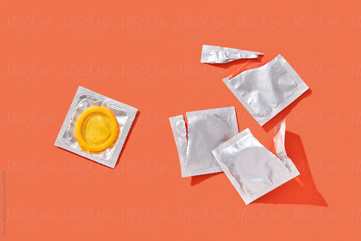 Yellow condom and empty condom packages on orange background.