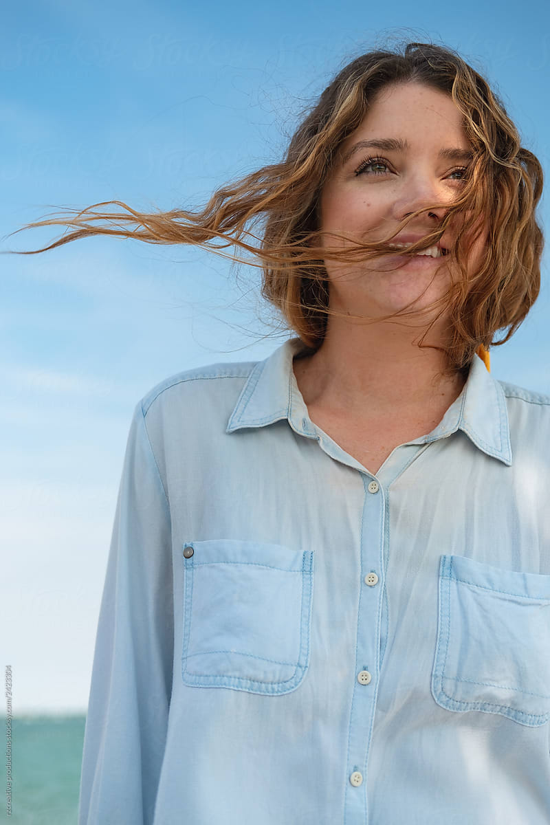 Portrait of a young brunette woman smiling as the ocean breeze blows through her hair.