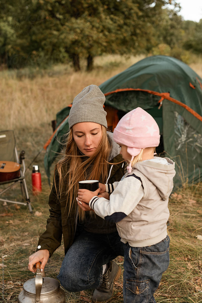 Mommy gives a mug with tea to her little baby girl while they\'re camping