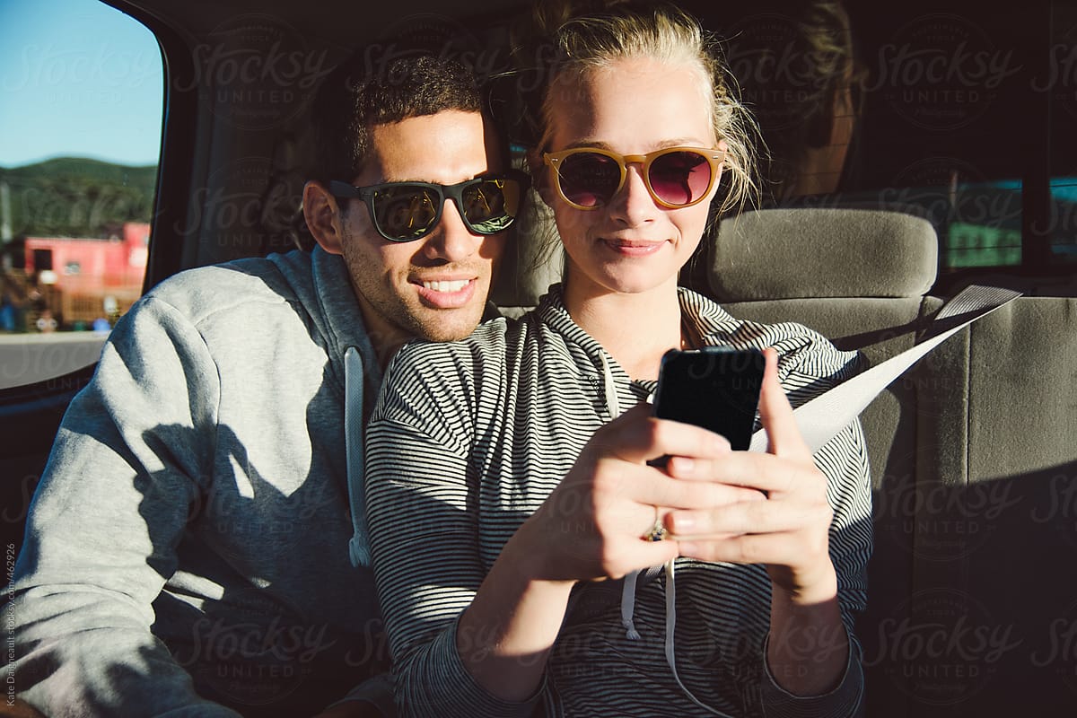 Guy and girl using smart phone in the backseat of a car.