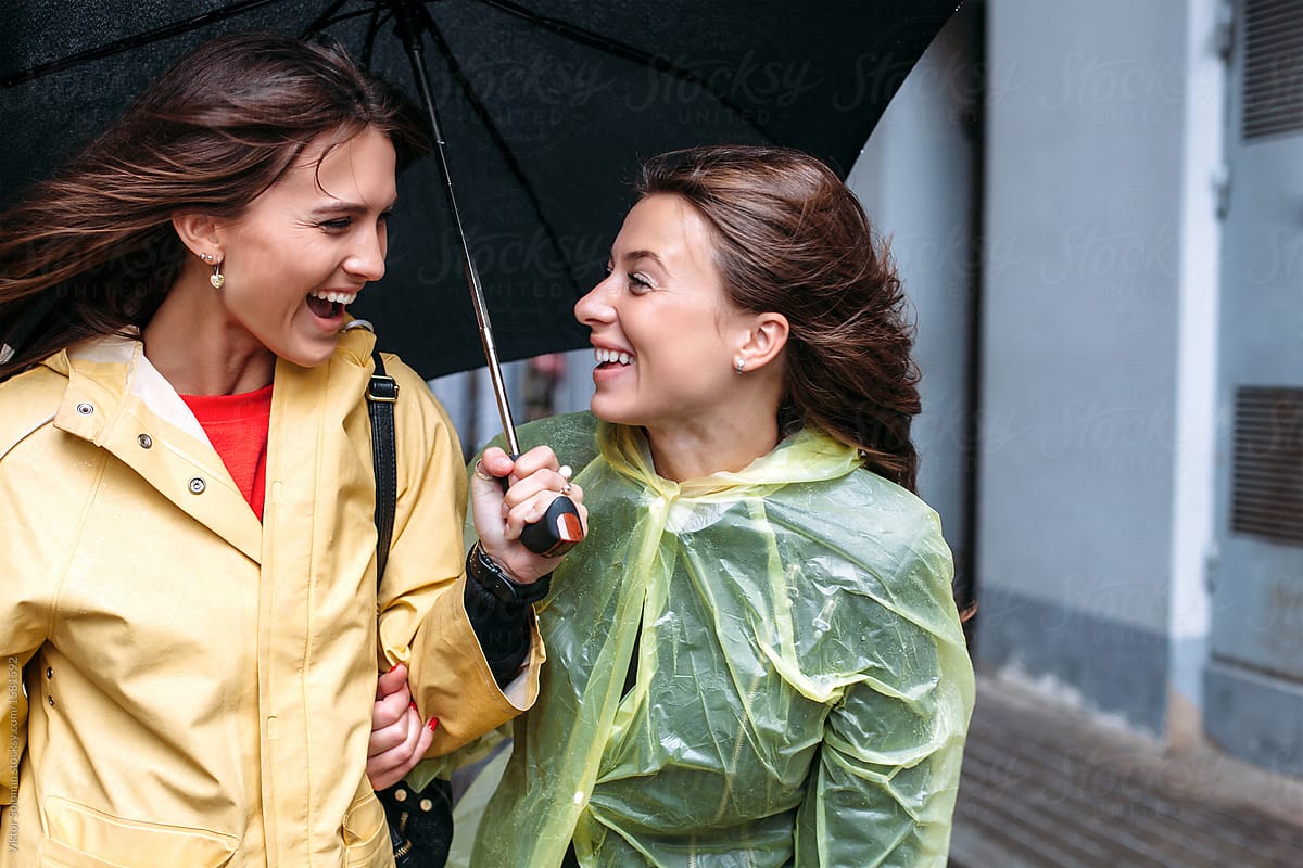 Pretty and funny happy stylish girls friends are walking at the street together under the rain have fun smiling and laughing