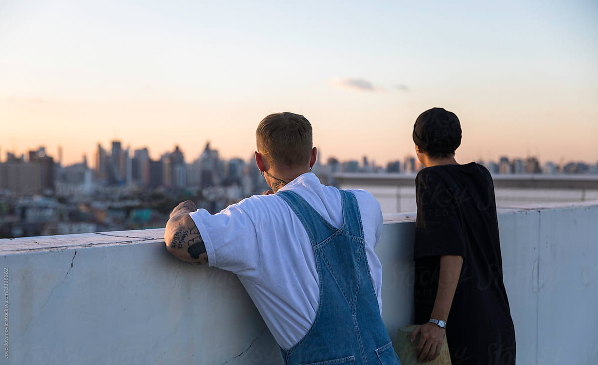 Two friends watching sunset over city from rooftop