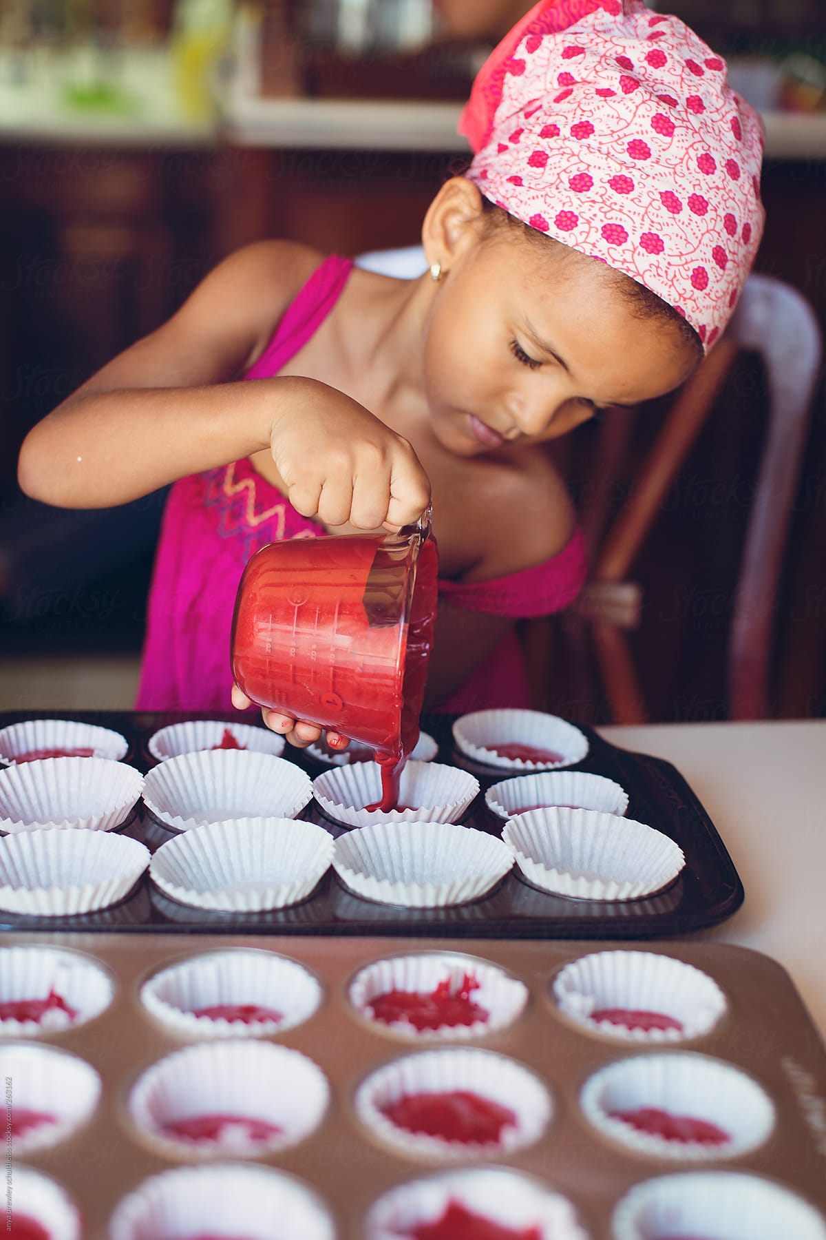 Young child pouring cupcake batter into a baking pan