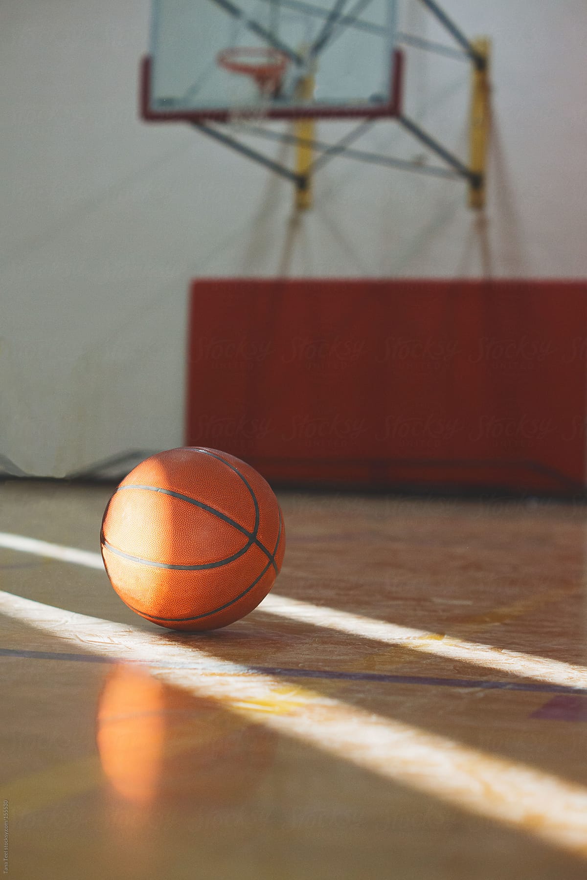 A basketball sits between sunbeams on a basketball court