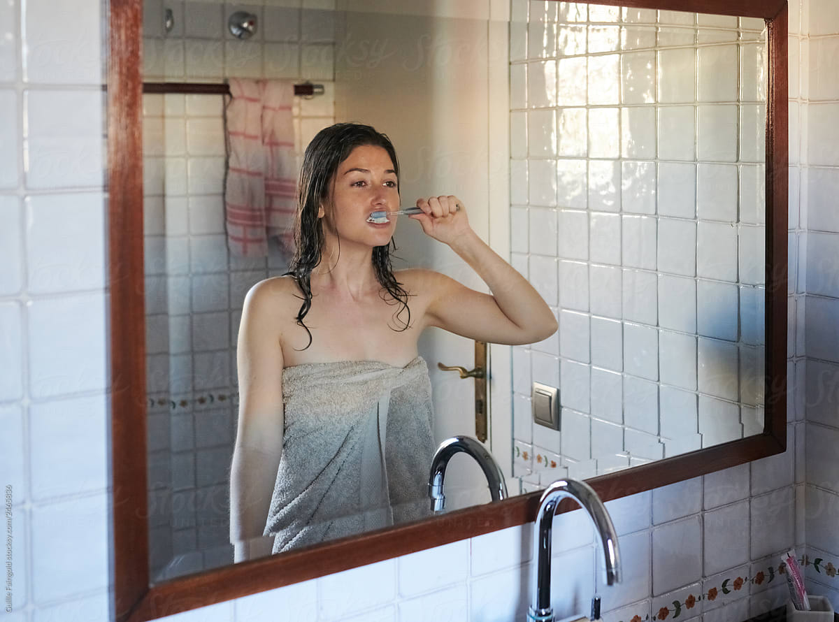 Woman in blanket brushing teeth in bathroom