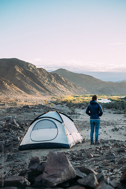 Hiker standing outside her tent in a rugged scenic desert landscape