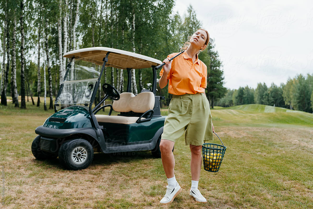 A woman is standing near a golf car on the course