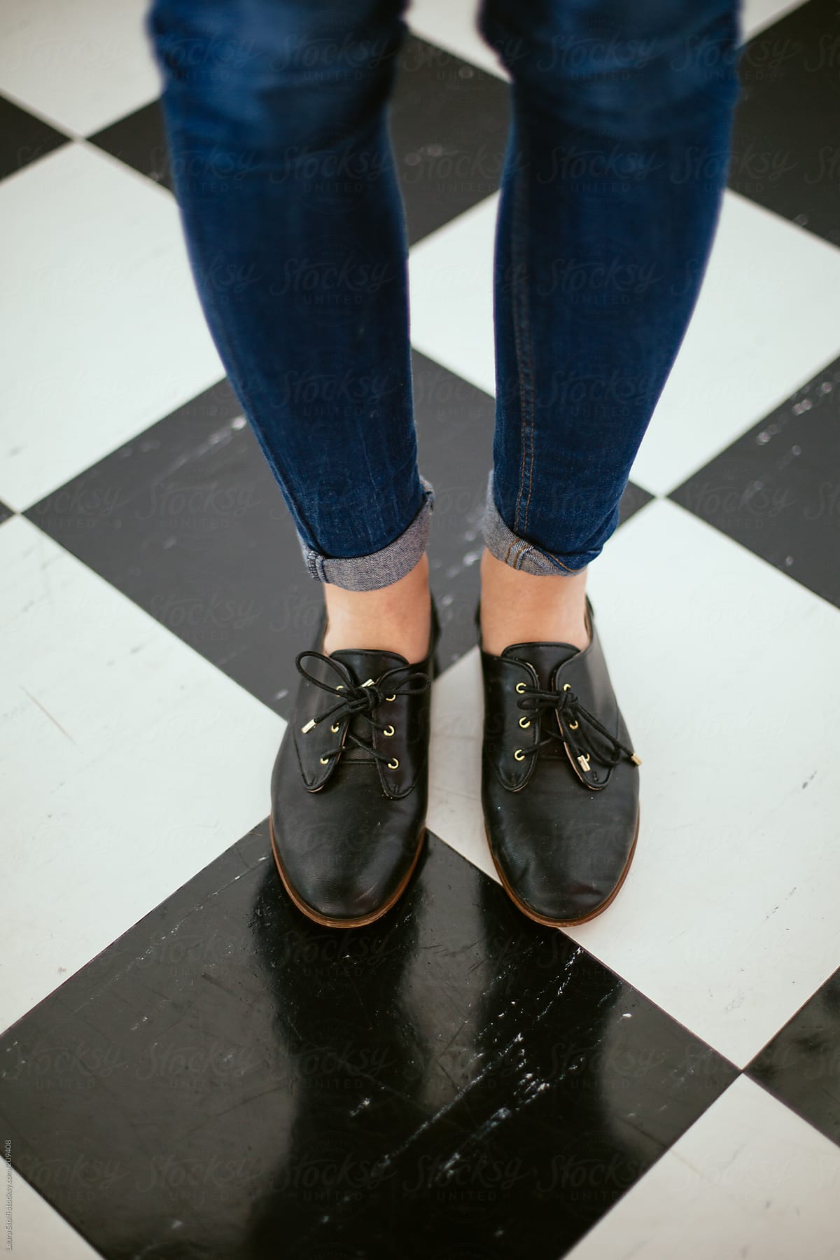 Girl wearing jeans and black leather lace-ups standing on checked flooring