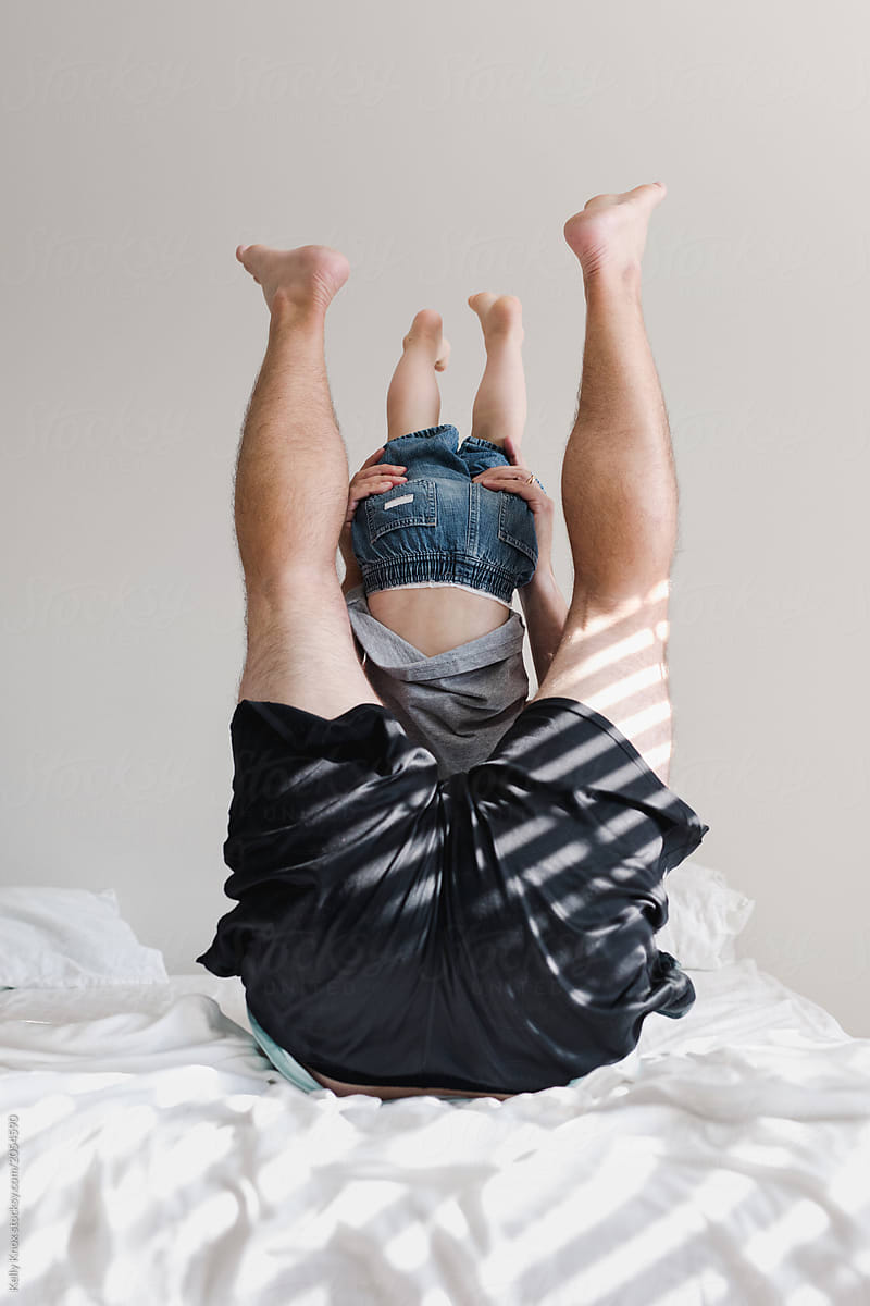 father and toddler son playing on a bed with legs up in the air