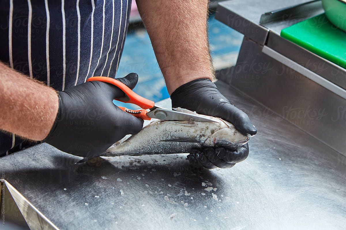 The hands of a male chef cut fish on a metal table. The process of cooking in the restaurant