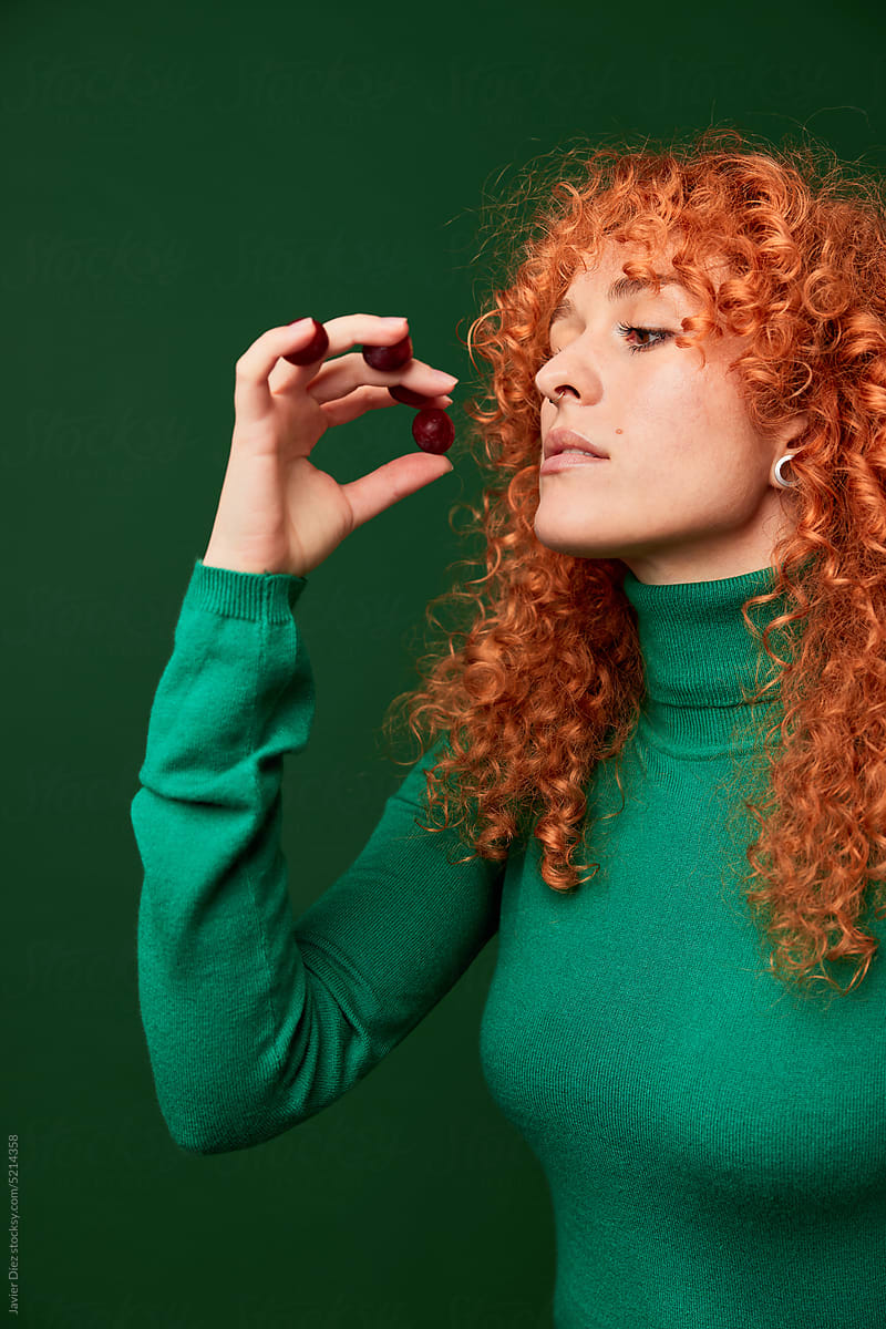 Ginger woman with cherries on green background