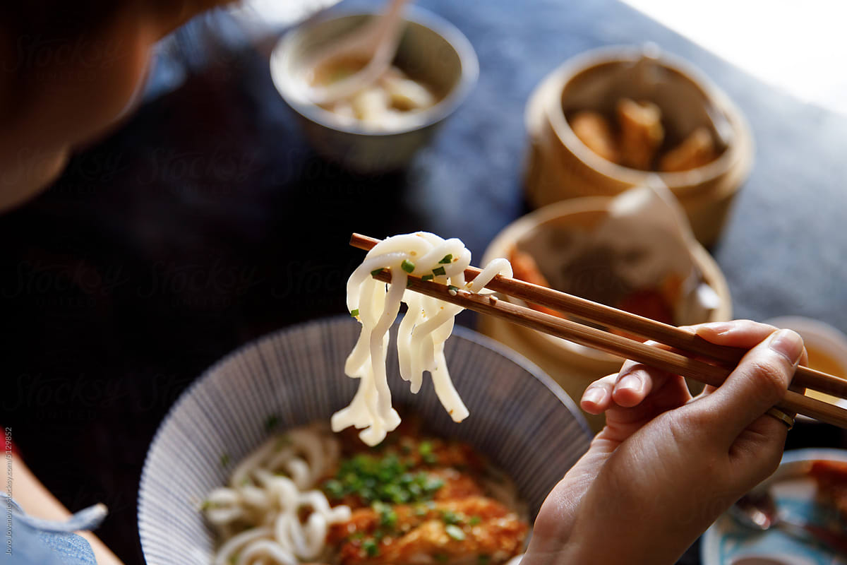 Hand of woman picking up noodles using chopsticks for eating