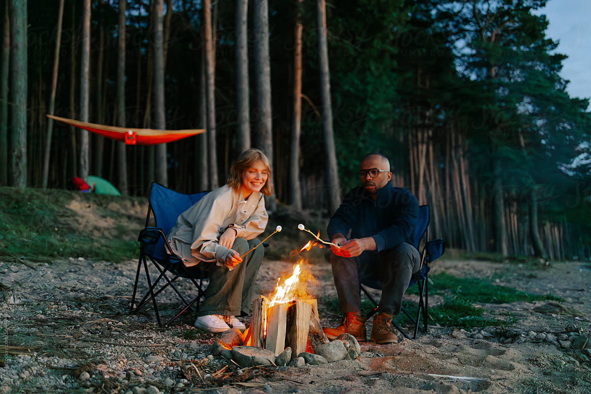 A man and a woman fry marshmallows in the woods