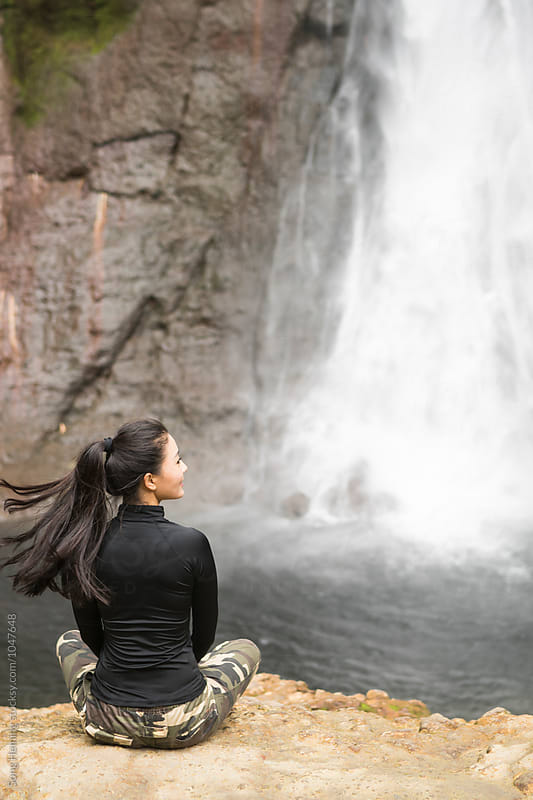 A woman sitting below a waterfall in the rain forest