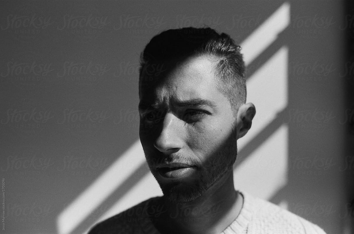 Portrait of young male with strong shadows on face in studio contrast environment