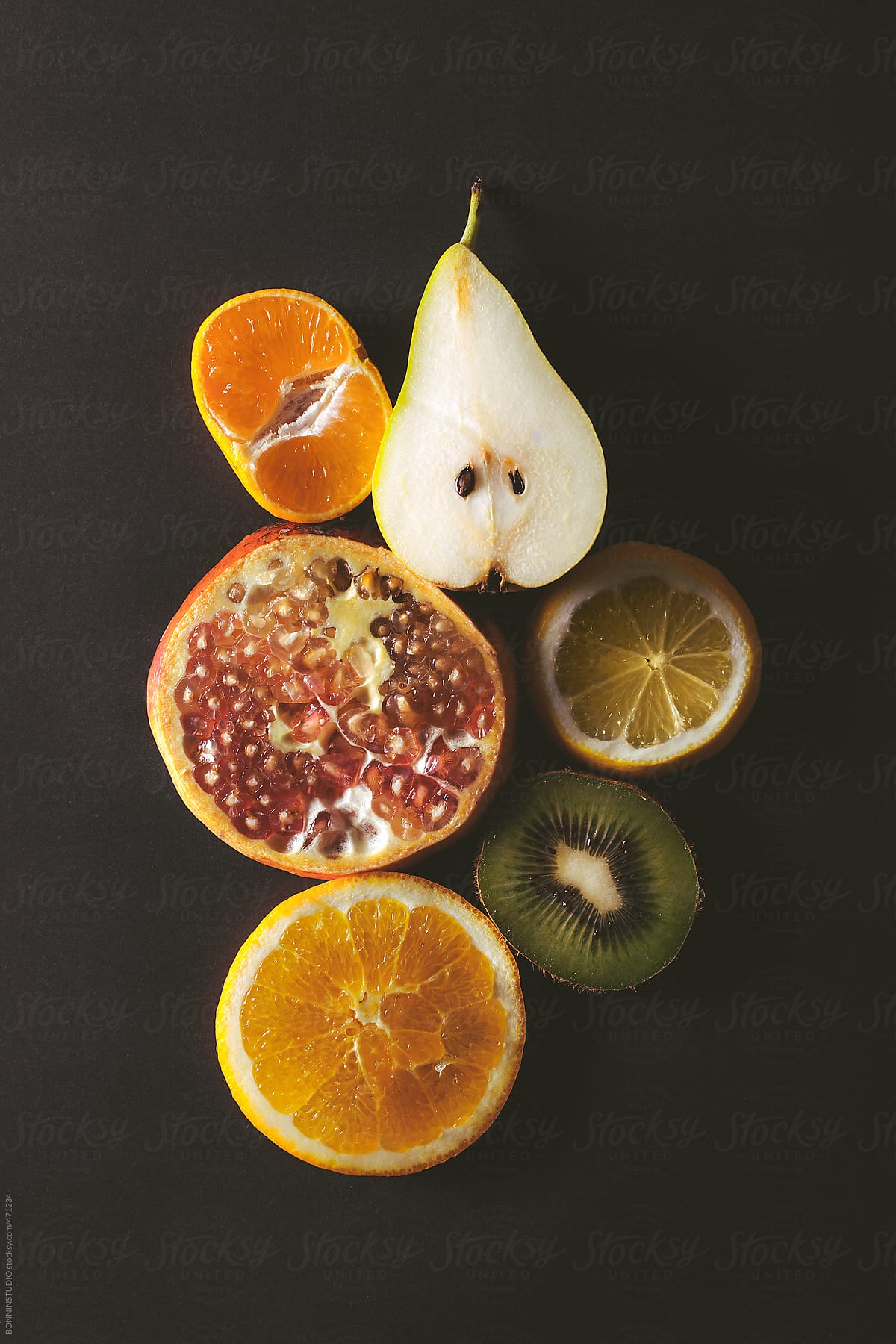 Overhead of sliced variety of fruits on black background.