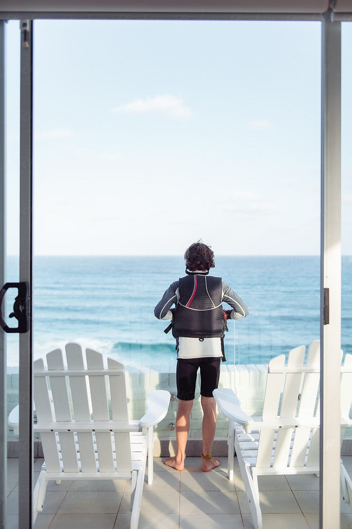 Child in sailing gear looks out at the ocean conditions