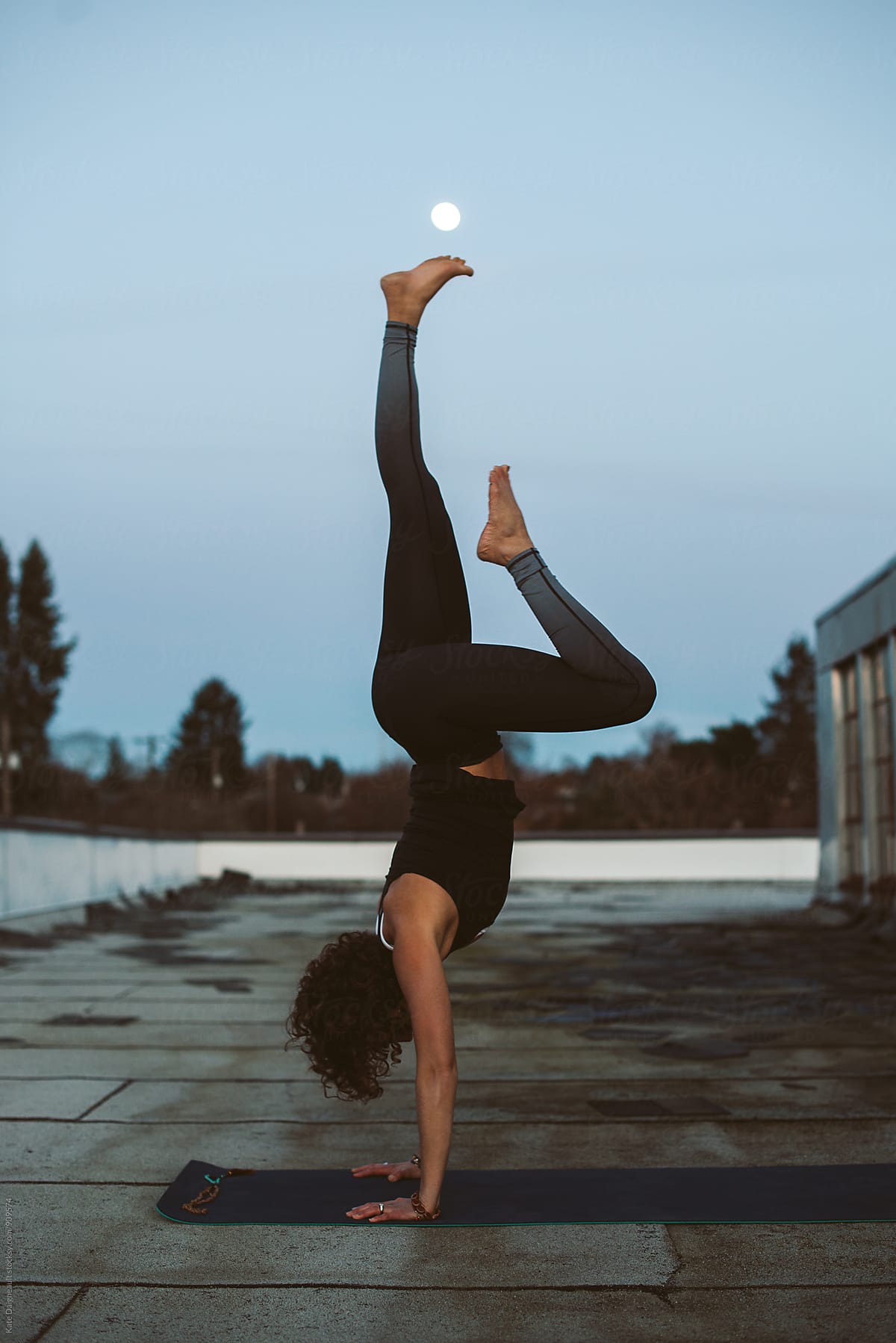 Beautiful young woman practices yoga on the roof of her loft under a full moon.