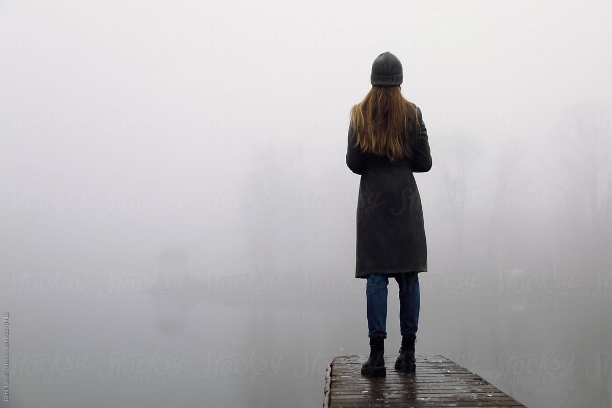 Stylish woman standing on pier on foggy day