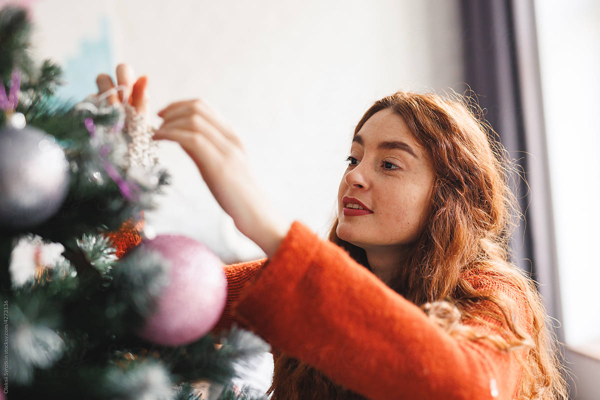 Adult girl hanging Christmas toy to top of conifer tree