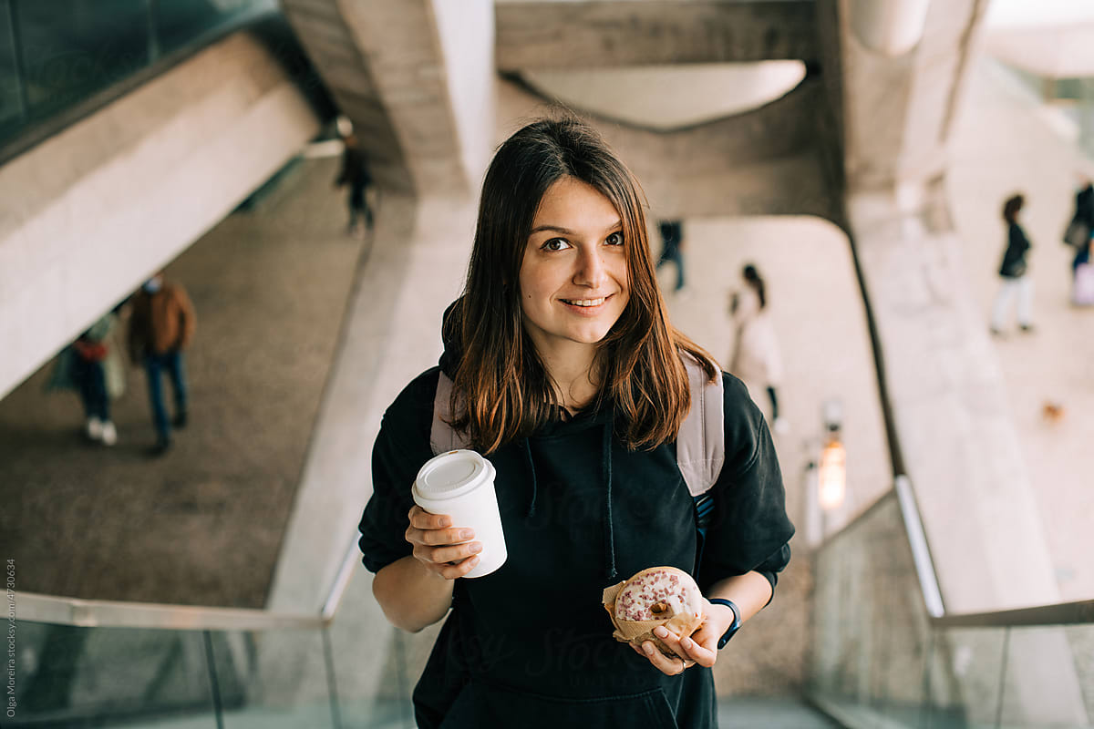 Smiling woman with coffee on the go and donut