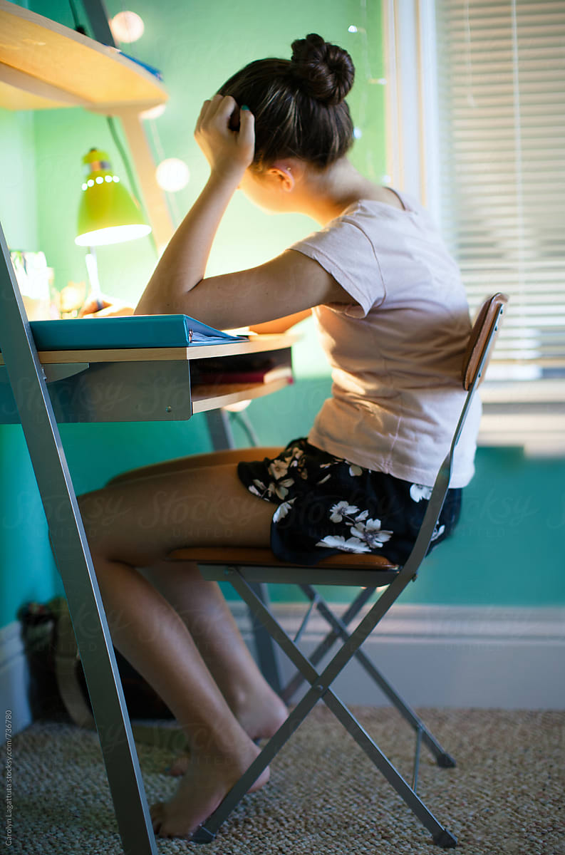 Teenage Girl Sitting At Her Desk In Her Bedroom Doing Homework By
